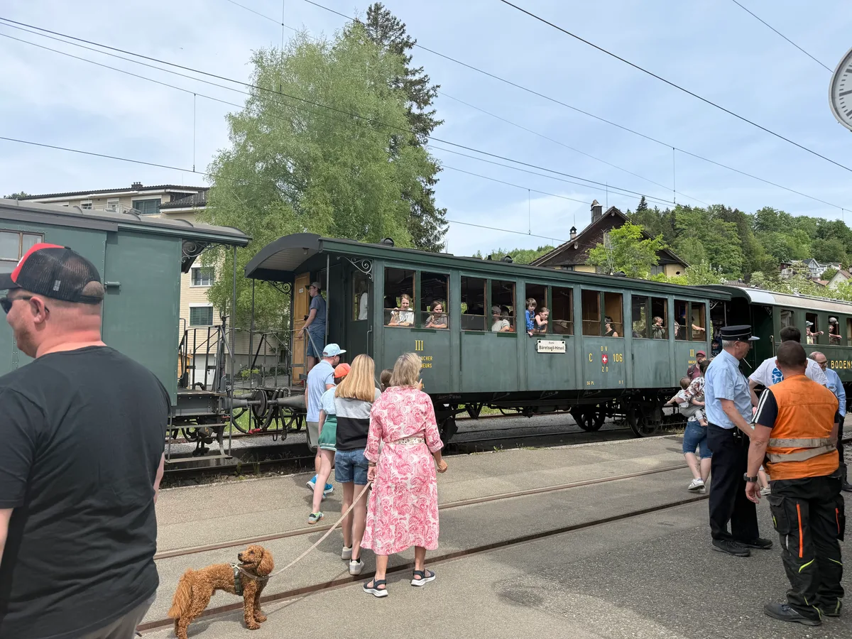 Besucherinnen und Besucher der Dampfbahn steigen beim Halt in Bäretswil aus, stehen neben den Gleisen oder verweilen im Zuginneren.